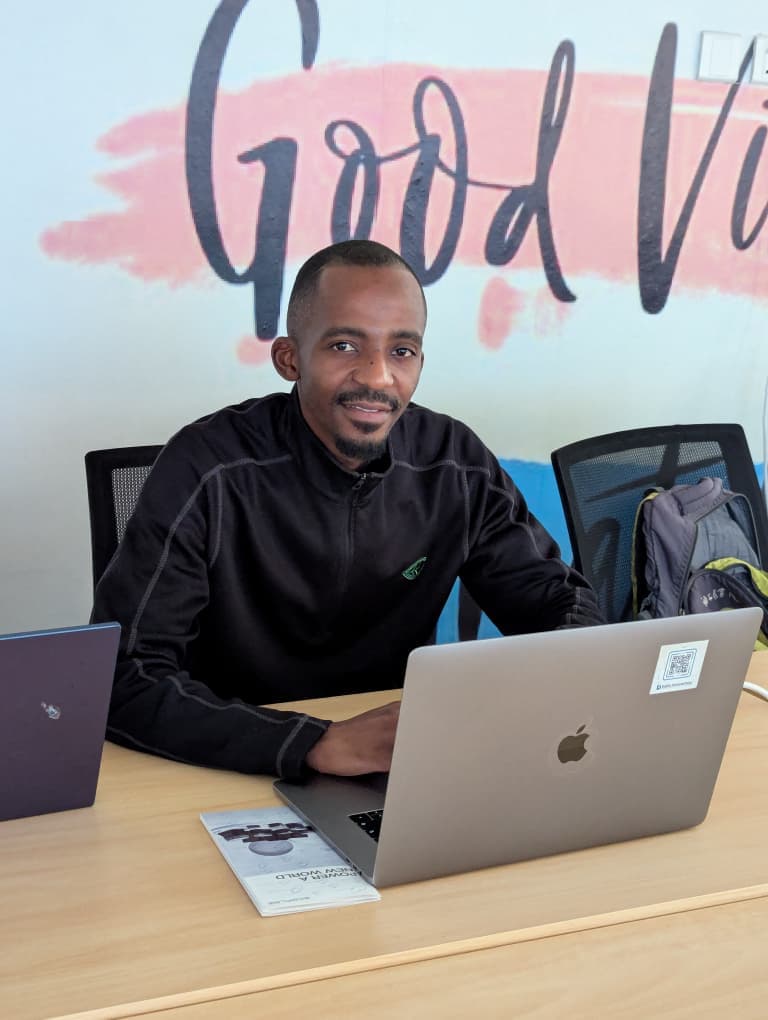 George M'sapenda working at his desk in front of a Good Vibes mural